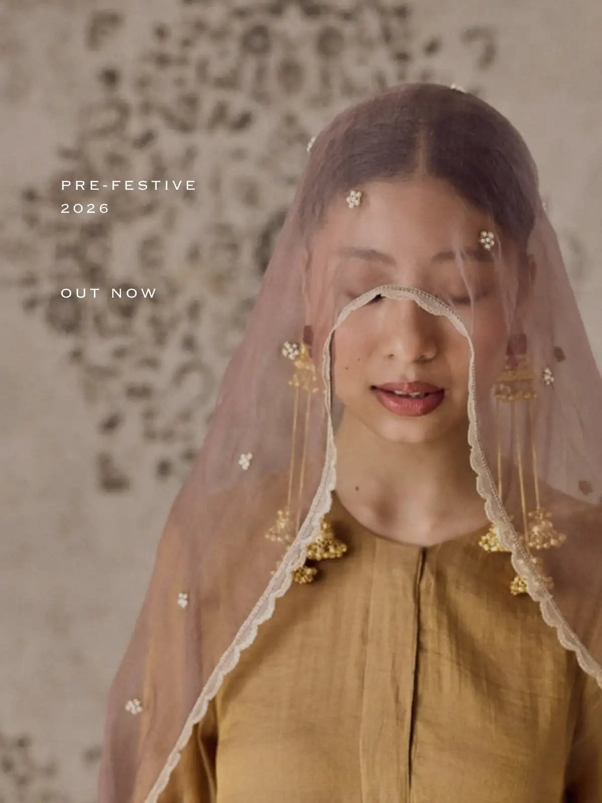 A delicate, sheer beige veil adorned with small white floral embellishments and gold-toned dangling ornaments.