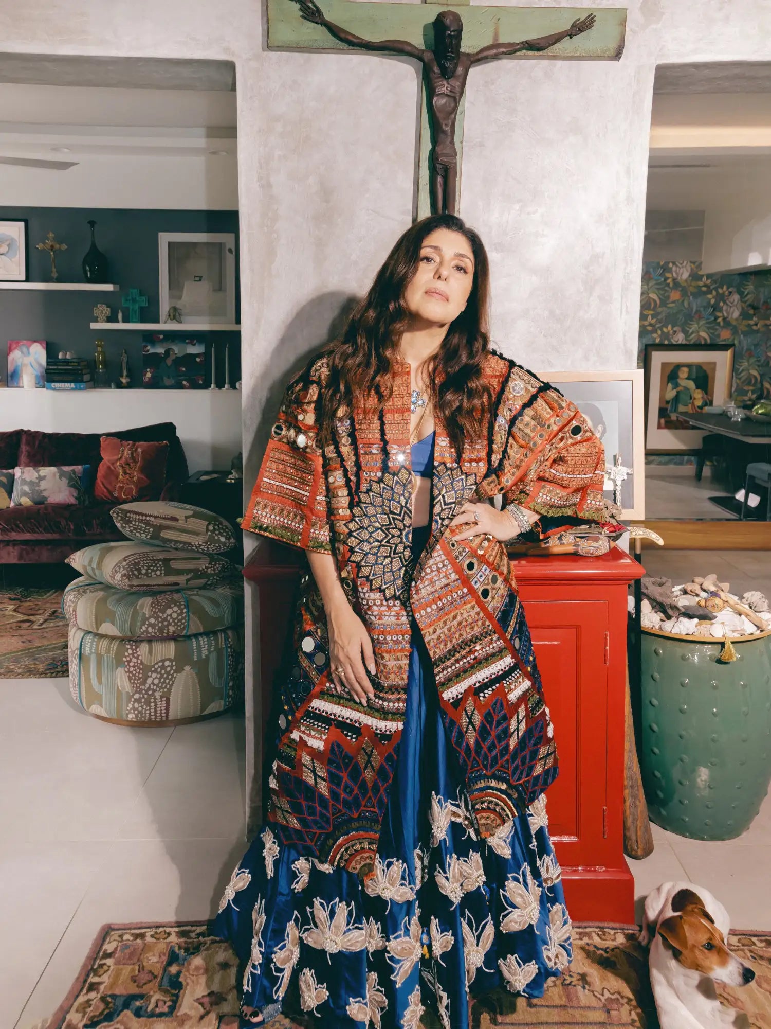 A woman wears a vibrant, intricately patterned orange and blue embroidered cape over a matching floral skirt.